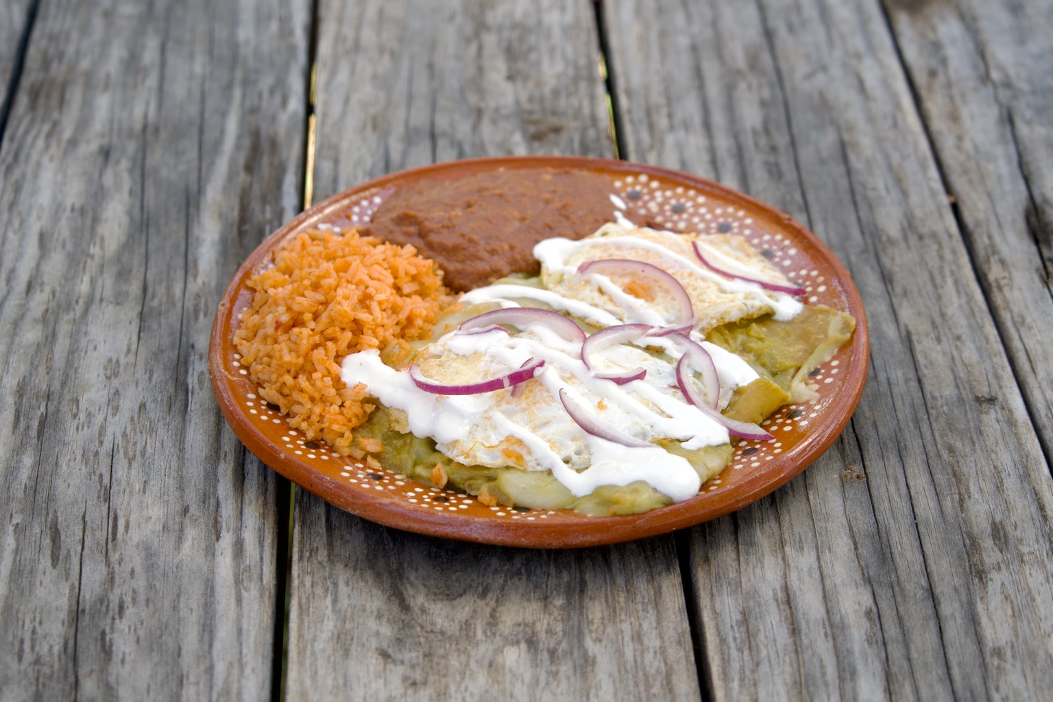 Green chilaquiles topped with eggs, crema, and red onion, beside rice and beans